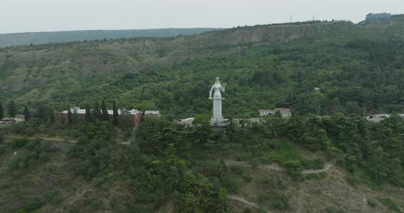 Slow aerial arc shot of the Mother of Georgia statue and Tbilisi landscape. alt