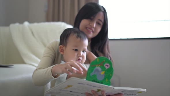 Young mother and little boy child reading book sitting on floor near sofa at home. Happy family.