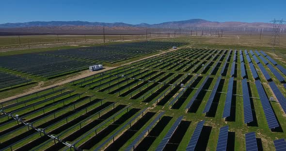 Aerial Over Solar Panel Field, with Mountains and Wind Turbines in Background