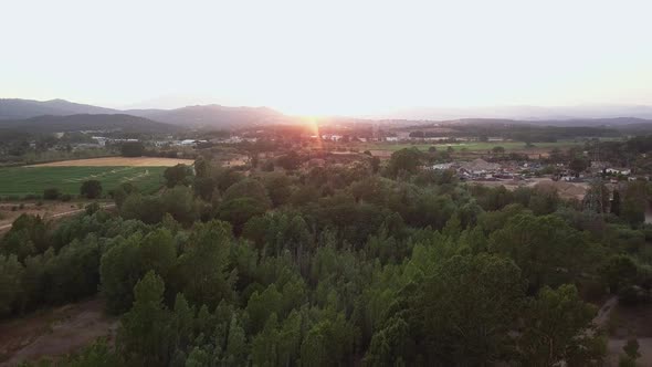 Aerial drone shot flying over a forest with fields on the left and a town on the right an a magnific alt