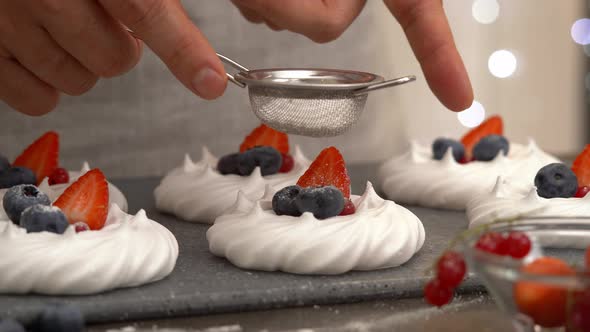 Hands Sprinkle Meringue with Blueberries and Strawberries with Powdered Sugar