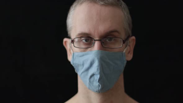 a Man in a Medical Mask and Glasses Nods His Head on a Black Background