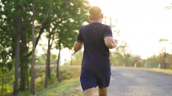 Sporty teenage boy running on natural park road with sunset time.