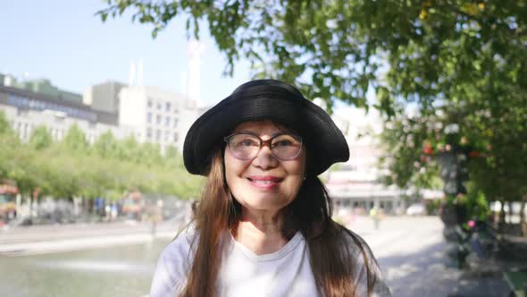 Front view of Asian woman standing and smiling in green city in Sweden alt