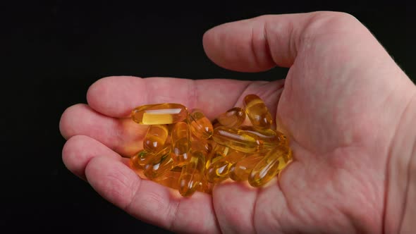 Caucasian Hand Holding Handful of Yellow Tramsparent Pills of Fish Oil on Black