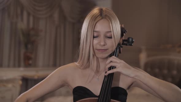 Blonde in a beautiful dress plays the cello. Cellist.