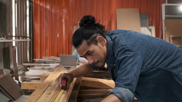 Young Asian man Carpenter uses a tape measure to measure wood on the workbench