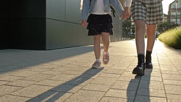 Two Schoolgirls of Different Ages with Backpacks Walk From School After School Holding Hands