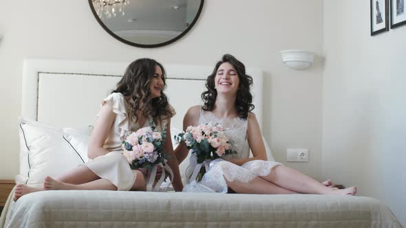 Two Girls with Flowers Sit on the Bed alt