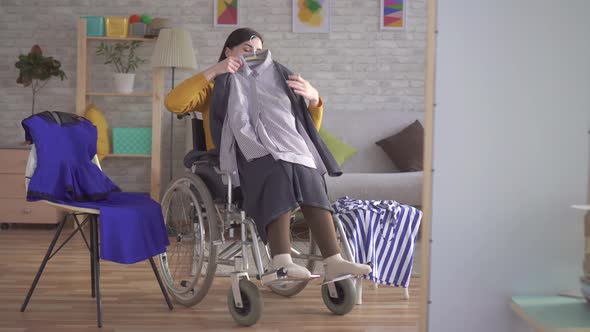 Young Disabled Girl in a Wheelchair Chooses Clothes for a Date in a Modern Apartment alt