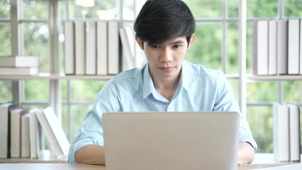 Young Asian business man working at home with laptop and papers on desk, working remotely alt