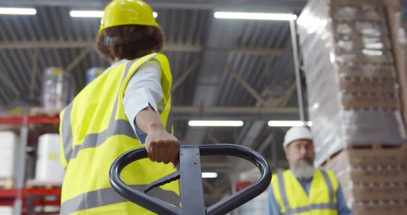 Back View of African Female Warehouse Worker Using Hand Pallet Truck alt
