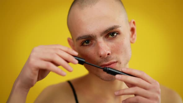 Closeup Portrait of Confident Queer Man Posing with Mascara at Yellow Background alt
