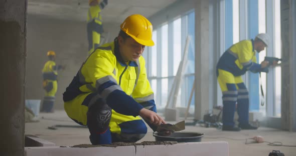 Construction Worker Using Trowel and Tools for Building Wall with Bricks and Mortar alt
