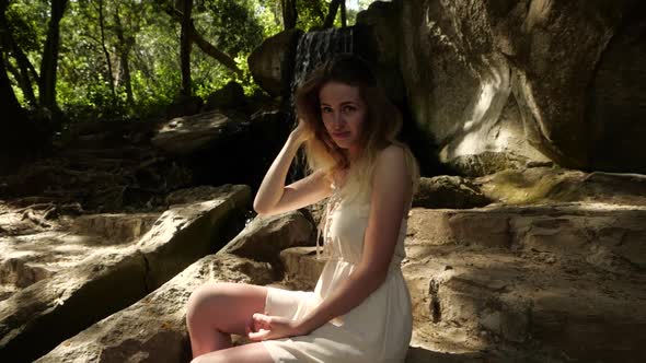 Cute Blonde Girl in White Dress Next To Waterfall alt