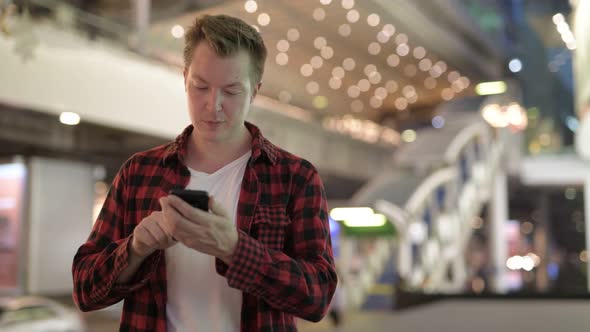 Young Happy Hipster Man Thinking And Using Phone In The City At Night alt