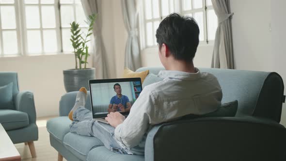 Man Greeting With Colleagues In Video Conference From Laptop At Home Living Room alt