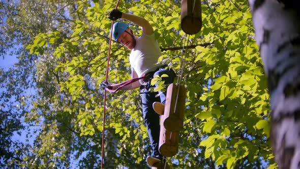 A Man Carefully Walks on Logs Suspended in the Air Between Trees in the Forest alt