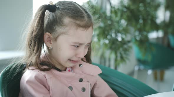 Little Girl Crying at a Table in a Cafe By the Window
