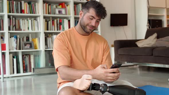 Happy Disabled Man with Prosthetic Leg Prosthesis Using Phone at Home alt