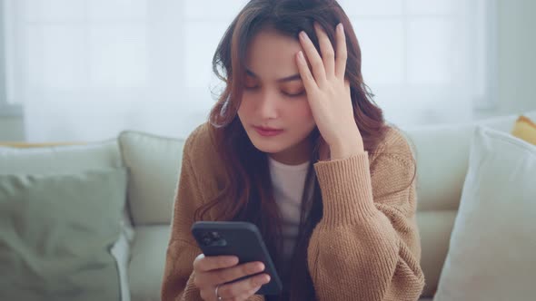 Upset young asian woman looking at mobile phone screen feels sad and disappointed alt
