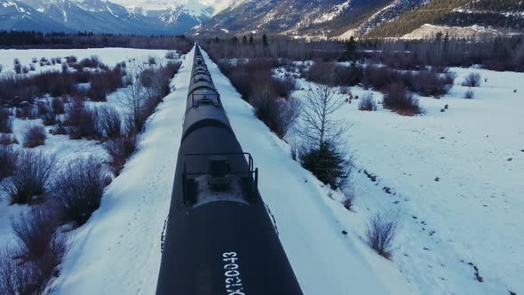 Train in a valley followed in winter snow oil tanks flyover alt