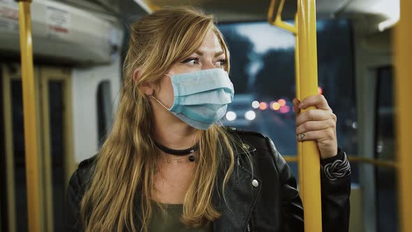 Young Girl Hipster in Protective Mask and Leather Jacket is Riding Tram Standing and Holding Onto alt