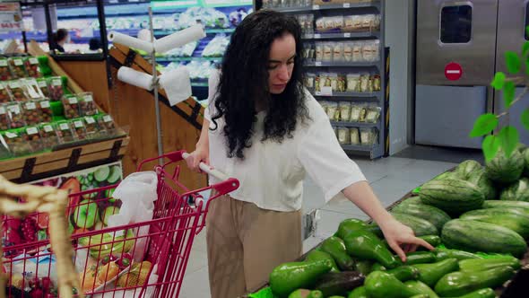Cute Woman in a Pink Suit Chooses in Grocery Choose Fresh Vegetables Avocado in Grocery Store alt