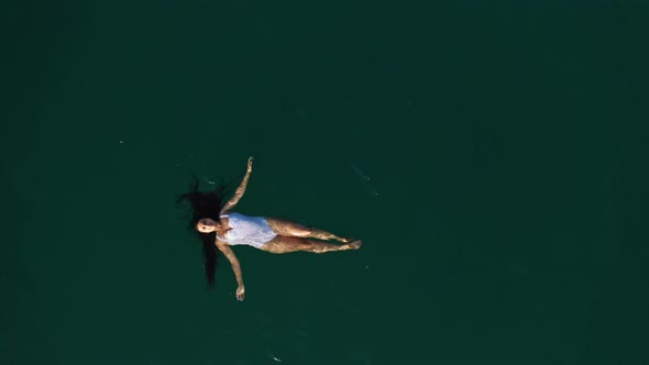 Top View of a Young Attractive Woman in a White Swimsuit Lying on the Water and Rowing with Her