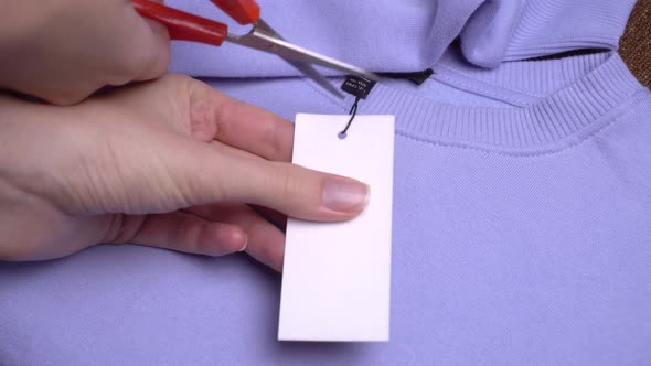 The girl's hands with scissors remove the price tag from the purple sweater. alt