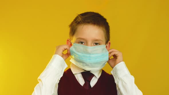Positive Caucasian schoolboy 7-9 years old takes off his medical protective mask and smiles alt