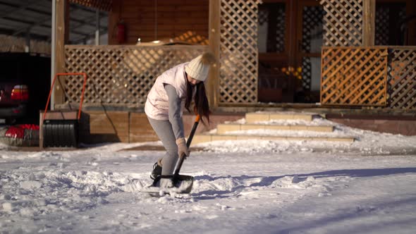 Young Woman Shoveling Snow on Backyard Near the House alt