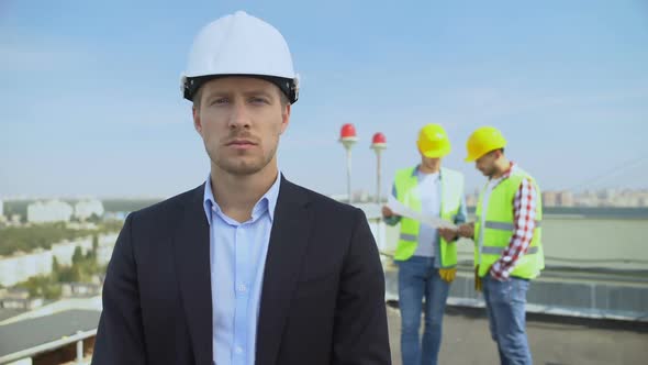 Male Architect in Helmet Looking Camera Standing Rooftop, Workers Background