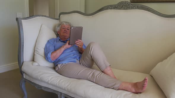 Caucasian senior woman using digital tablet while sitting on the couch at home alt
