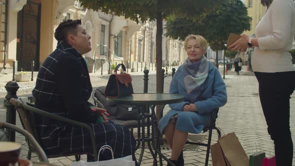 Elderly Female Friends Sitting Placing Order to Waitress Outdoors alt