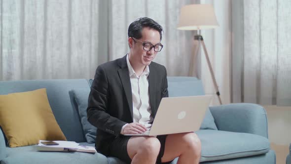 Asian Businessman In Jacket And Shorts Having Video Call On A Laptop At Home alt