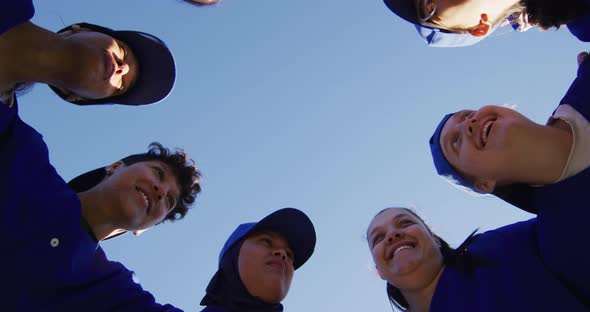 Low angle view of diverse group of female baseball players in a huddle against blue sky alt
