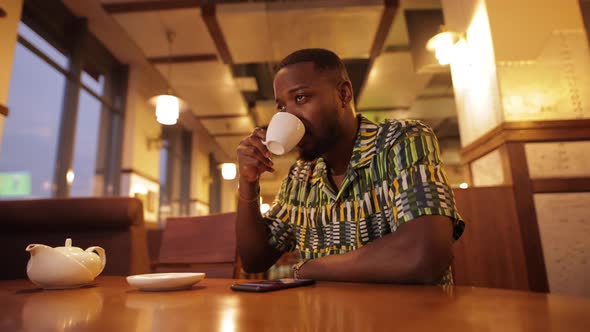 AfricanAmerican Man Looking in Smartphone and Drink Coffee