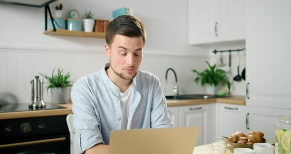 Man Talks Online By Video Call on Laptop in Kitchen, Eating Breakfast in Morning