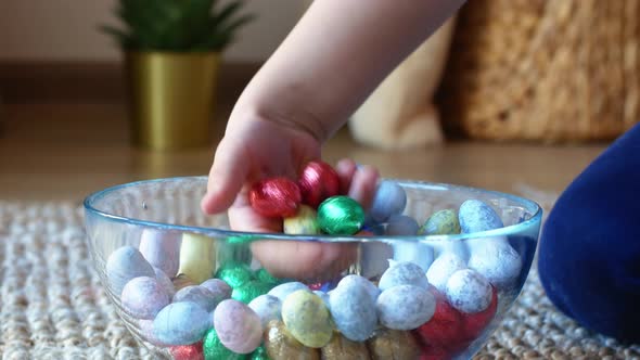 A child plays and chooses small, colorful Easter eggs in a glass dish on a wicker rug