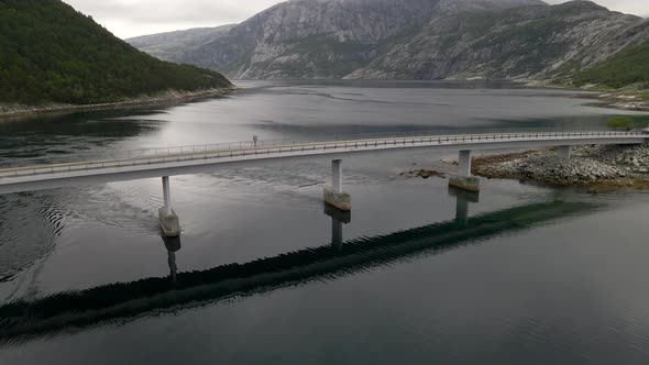 Aerial shot of a bridge as a car drives over with lake and mountain backdrop, Norway alt