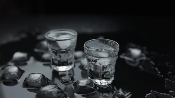 Add Ice Cubes To Shot of Vodka in Glass Against Black Background. Alcohol Drink alt