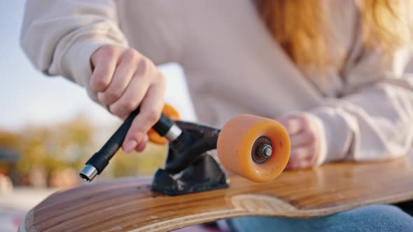 Close Up of Unrecognizable Skateboarder Girl Unscrewing Wheels on Her Longboard with Allen Key or alt