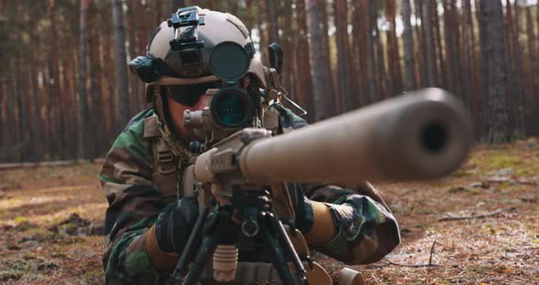 A Bearded Soldier Lies on the Forest Litter in a Tactical Military Uniform with a Helmet on His Head alt