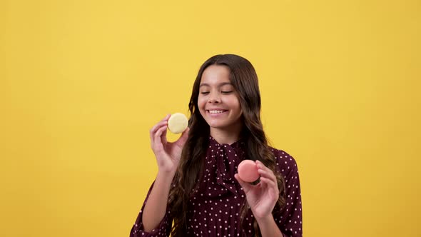 Happy Playful Girl Child Hold Macarons at Eyes Sticking Tongue Out Yellow Background Sweettooth alt