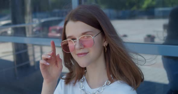 Portrait of Stylish Young Girl Smiling at Camera When Correcting Sunglasses alt