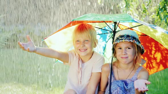 Two Cheerful Girlfriends 5 Years Hiding From the Rain Under an Umbrella Rainbow Colors. Happy alt