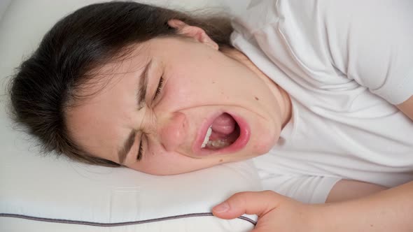 A 30Yearold Brunette Woman Yawns Lying on a Pillow on Her Bed alt