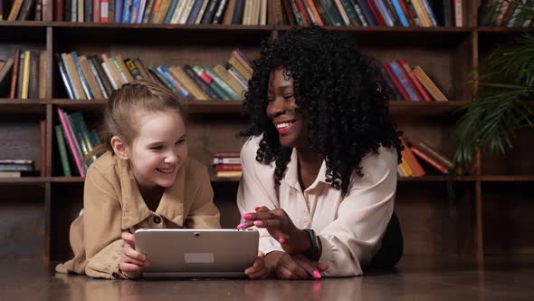 Schoolgirl and Babysitter Look at Tablet Display and Laugh alt