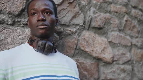 A Young Black Student with Headphones Walks Through the City Centre at Sunset